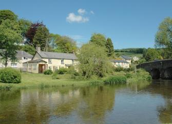 An Exmoor holiday home on the banks of the calm River Barle flowing under a stone bridge.