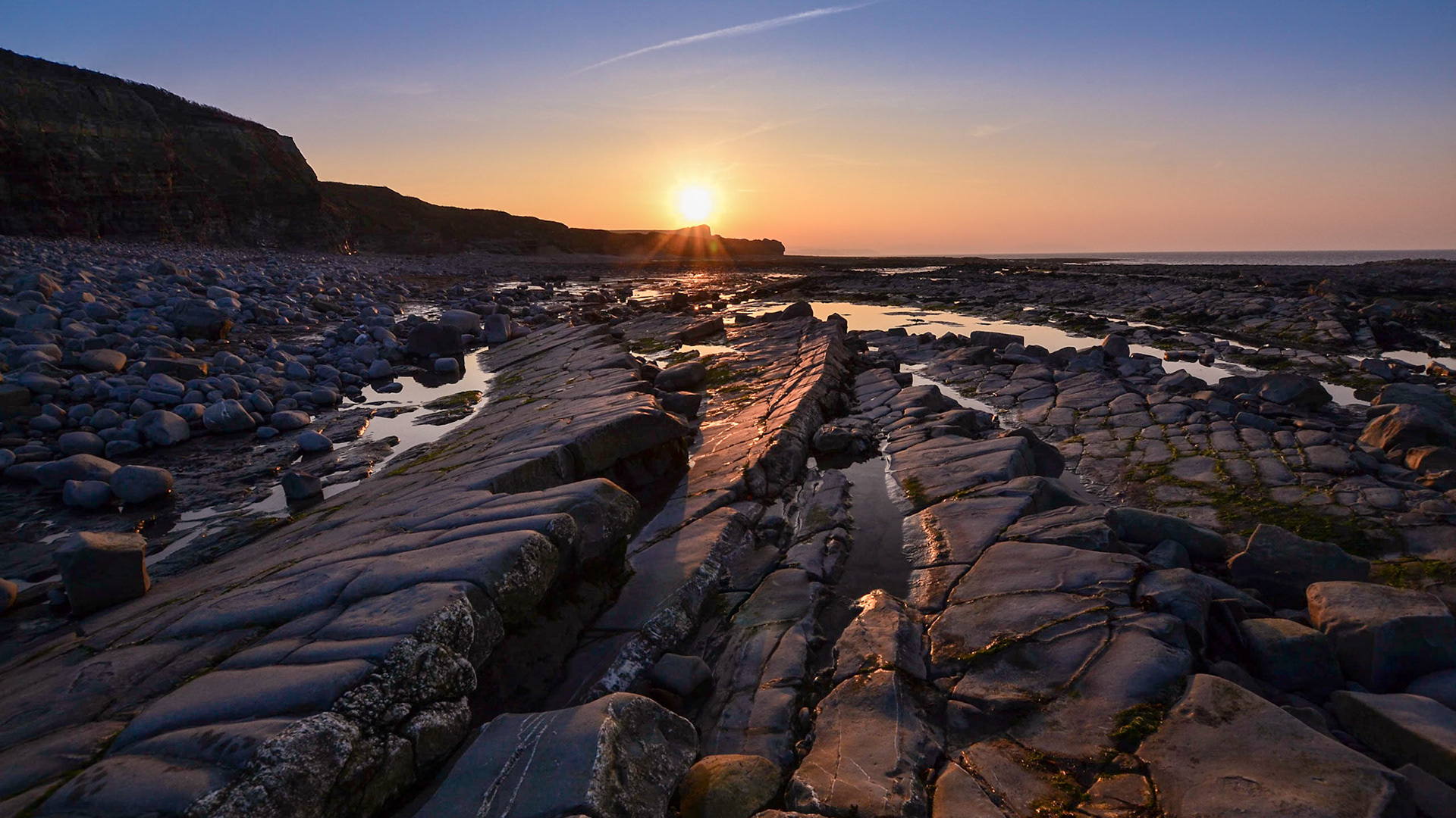 A summer sunset on Kilve beach at low tide shows rows of jagged rocks.