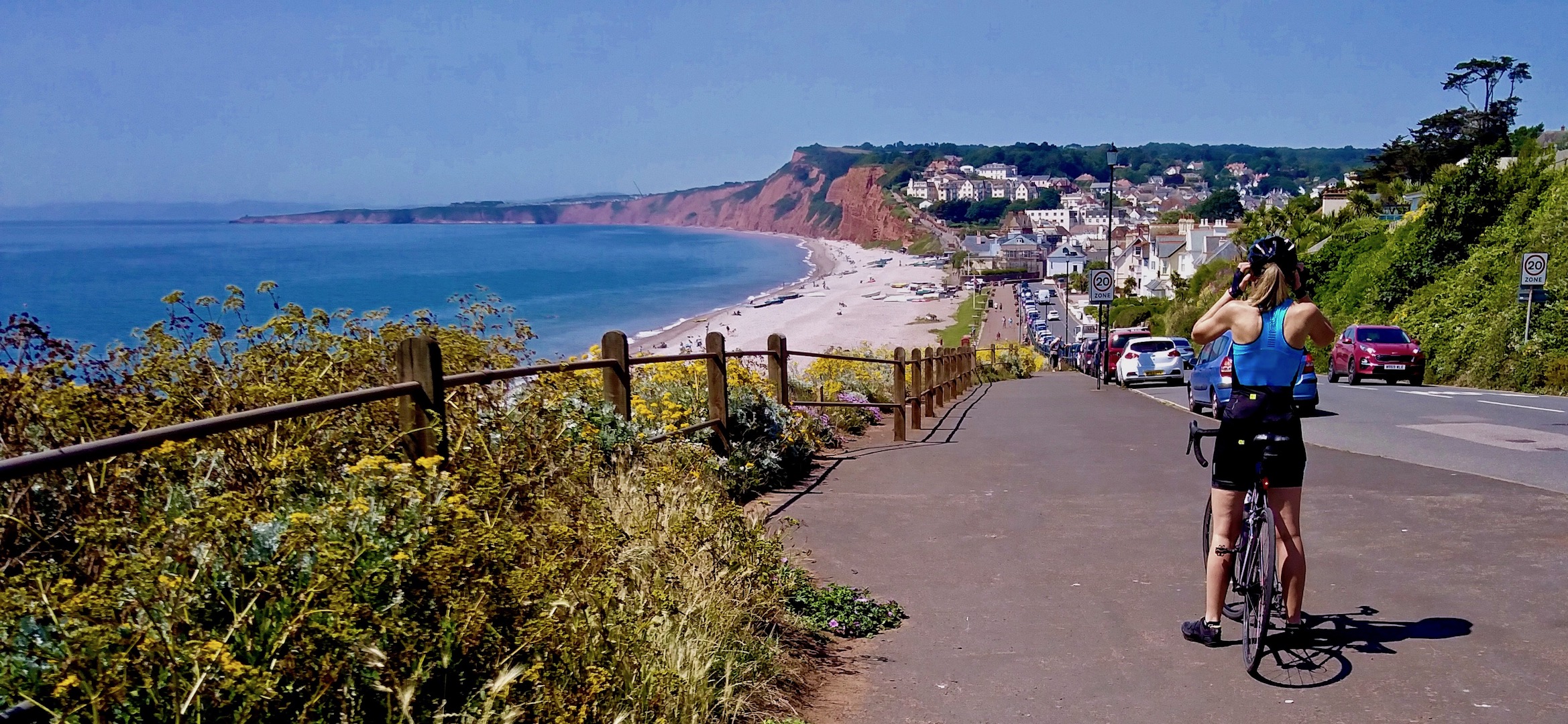 A cyclists gazes down a hill to a wide beach nestling between headlands at Budleigh Salterton.