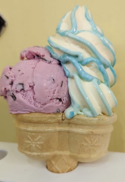 A twin cone ice cream cornet with two scoops covered in whipped cream and green 'sauce'.