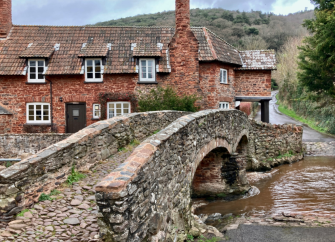 An ancient twin-arched packhorse bridge spans a brook in an Exmoor village.