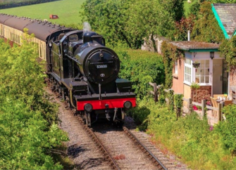 A steam engines pulls its carriage past a lineside holiday cottage on the West Somerset Railway
