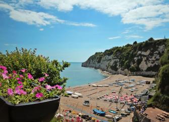  A large shingle East Devon beach in a cove surrounded by tall cliffs. Small fishing boats lie on the beach.