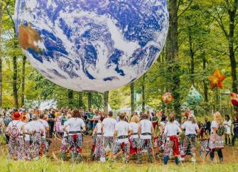 festival goers an garish attire admire a large inflatable globe hanging from woodland trees i