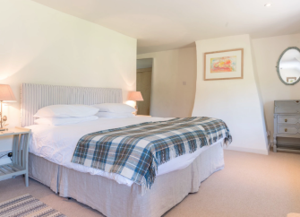 A spacious cottage bedroom with a large double bed, tartan bedspread and carpeted floor.