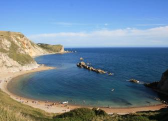 Lulworth Cove in Dorset: A horseshoe-shaped bay lined by cliff-tops and a sandy beach on a summers day.