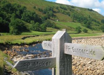 A wooden finger post for footpaths alongside a shallow river.