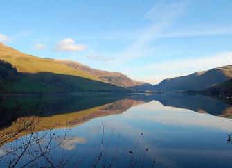 Calm waters reflect the land in an autumnal view of a reservoir at sunset