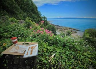 water colour paintings resting on an ivy-covered stone wall with a  sea view in the background