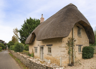 A thatched country cottage overlooks a quiet country lane in the Cotswolds.