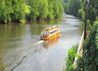 A small cruise boat makes its way upstream around a tree-lined River Wye.