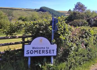 A 'Welcome to Somerset' sign on a quiet, winding country lane.