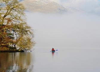 A holiday cottage overlooks a large lake in front of tall Lake District Fells.