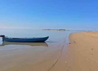 A rowing boat anchored at the waters edge on a long sandy beach in North Devon.