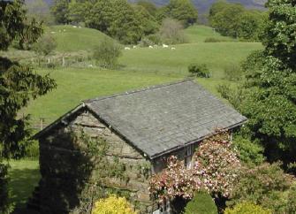 A stone-built barn conversion with rose-covered walls stands between trees with an open field at its rear.