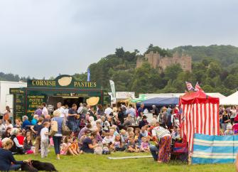 Families at Dunster Show watch a Punch and Judy show with Dunster Castle in the background