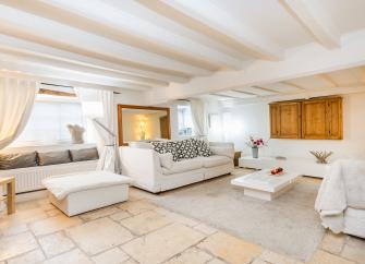 A large holiday cottage lounge with beamed ceiling, comfortable sofas, cushioned window seats and a large-screen TV..