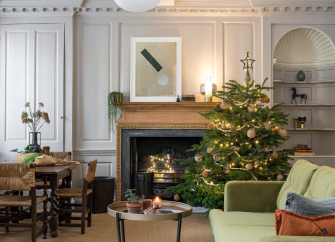 A luxur lounge at Christmas with a large fireplace, dining table, sofa and decorated pine Christmas tree.