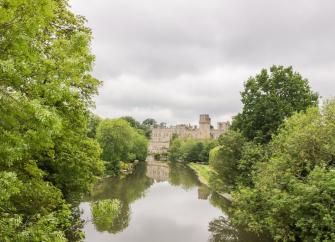 The wide River Avon flows placidly between tree-lined banks towards Warwick Castle 