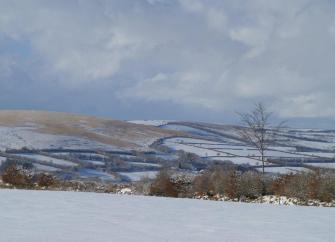 A winter view of a snow-covered Exmoor landscape which lies beneath dark, snow-laden clouds