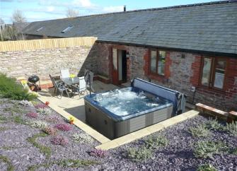 Single storey exterior of a barn conversion with a hot tub on its terrace.