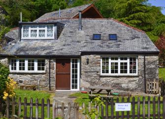 Exterior of a stone built holiday home ner Bodmin with a slate roof and a wider dormer and two velus windows overlooking a lawned and picket fence.