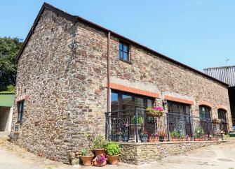 Exterior of a stone-built barn conversion in Bideford with large floor-to-ceiling windows on the ground floor overlooking a courtyard with flower pots lining the wall.