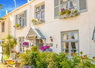 Exterior of a double-fronted Torquay holiday cottage with a small overhead porch and flower-filled front garden.