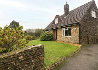Exterior of a stone-built Dorset chalet bungalow overlooking a front lawn and drive.