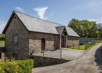 Exterior of a stone-built barn conversion with a securely fenced lawn and level access from the parking spaces.