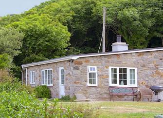 An Anglesey bungalow surrounded by lawns and a woodland backdrop.