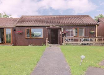 A single storey holiday bungalow with a patio and large lawn.