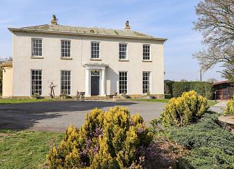 A classic country house with a pillared front entrance and surrounded by lawns and mature flower beds