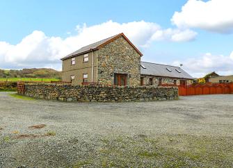 A Welsh stone-built barn conversion surrounded by a low stone wall in a large courtyard.