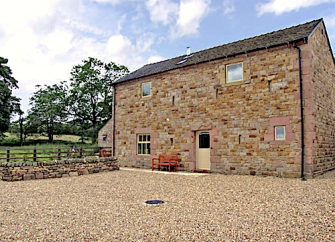 A stone-built, 2-storey Staffordshire barn conversion overlooking a shingled parking area and a fenced-in lawn.