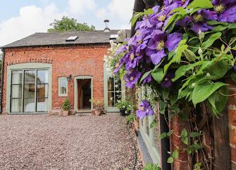 A flowering vine cimbs the walls of aconvrted coach house overlooking a courtyard in Shropshire