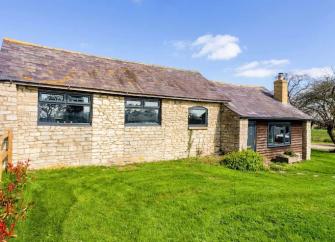 A single storey, stone-built Cotswold holiday bungalow in Oxfordshire overlooks a large lawn.