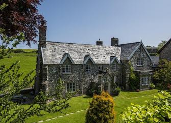 A large stone-built Exmoor cottage surrounded by trees and open fields.