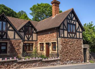 Exterior of an L-shaped country cottage with timbered gable end overlooking a country lane in Dunster.