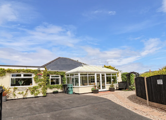A bungalow with a large sunroom overlooks a drive with plenty of parking space