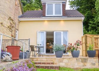 A semi-detached chalet bungalow with French Windows onto a patio with steps down to a flower-lined lawn.