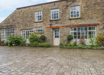Exterior of a 2-storey, stone built holiday cottage in Cumbria with traditional cottage windows.