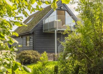 A clapper-boarded barn conversion with steps to a balcony half-hidden between trees.