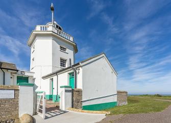 Exterior of a lighthouse holiday cottage and small tower on a grassy clifftop