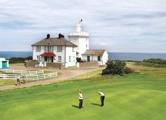 A lighthouse on the edge of a golf links with sea views in the background.