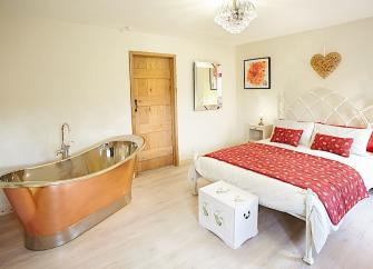 A spacious double-bedroom with a bed and deep, polished copper bath.