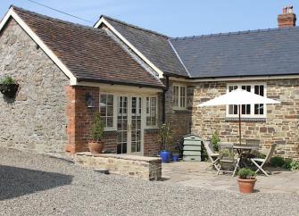 Exterior of a single-storey, stone-built cottage with a patio containing a dining table and chairs.