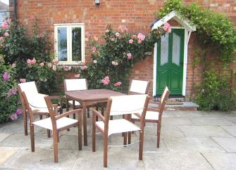 Exterior of  brick-built cottage clad with a rambling rose and overlooking a paved area with dining tsable and chairs