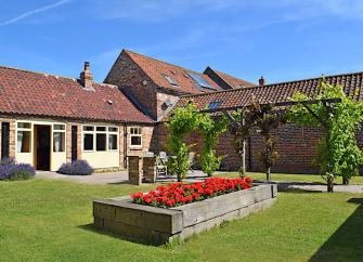 Barn conversion buildings overlooking a grass courtyard with a raised flower bed.
