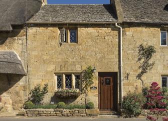 Exterior of a 2-storey, Cotswold 'honey stone' cottage with mullioned windows.